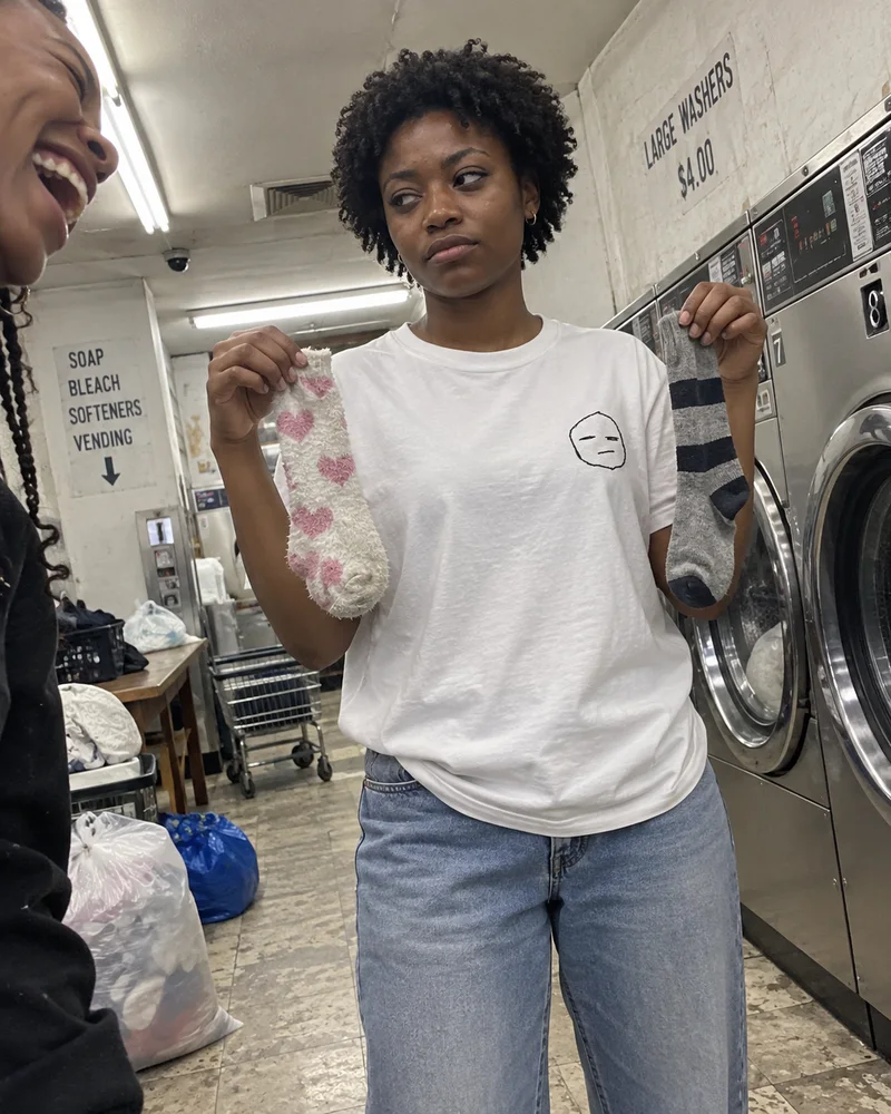 Studio concept: a woman comparing mismatched socks with a tired face stitched on her white tee