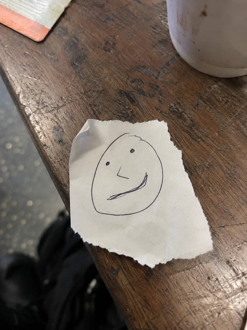 Studio concept: an awkward pen face on a torn café paper scrap, with a deliberately crooked broad mouth