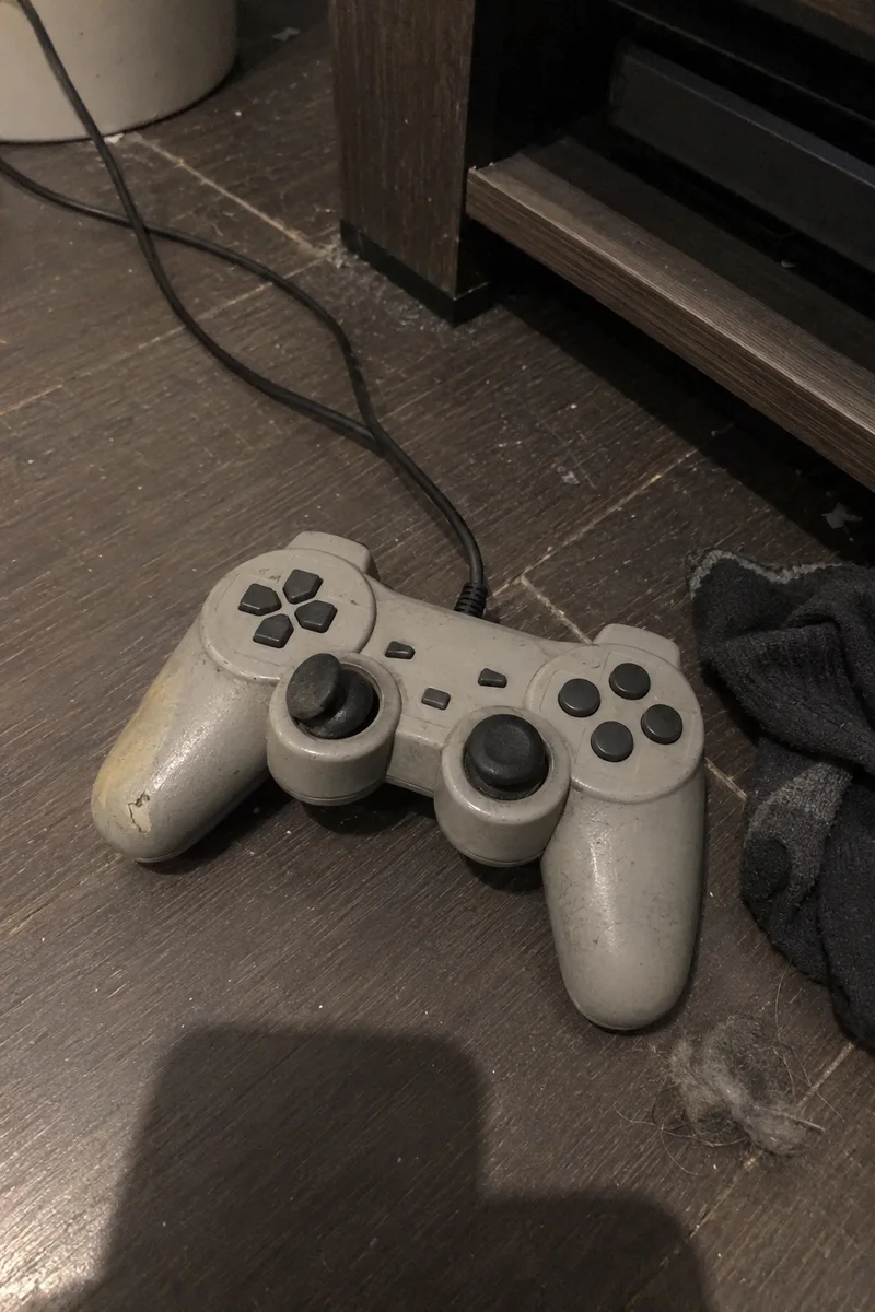 Studio concept: a scuffed grey wired game controller with a left stick resting off-centre