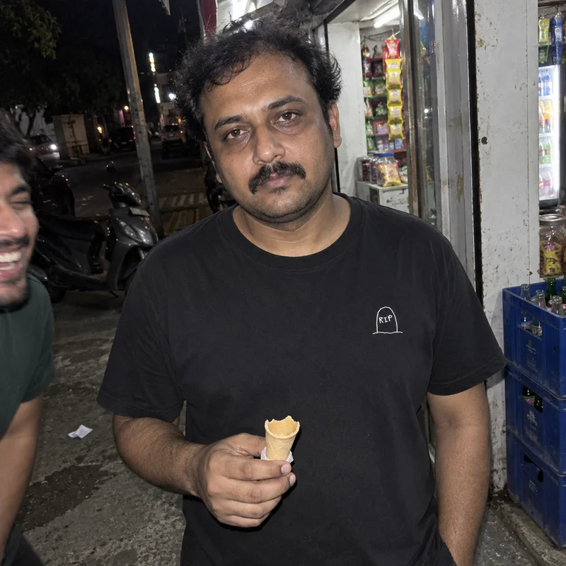 Studio concept: a friend holding an empty ice-cream cone outside a shop at night, wearing a tiny RIP embroidery