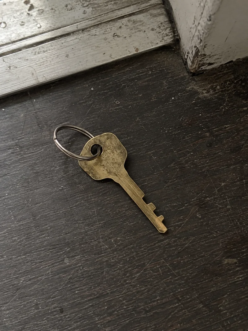 Studio concept: a worn brass apartment key on a ring by a scuffed threshold