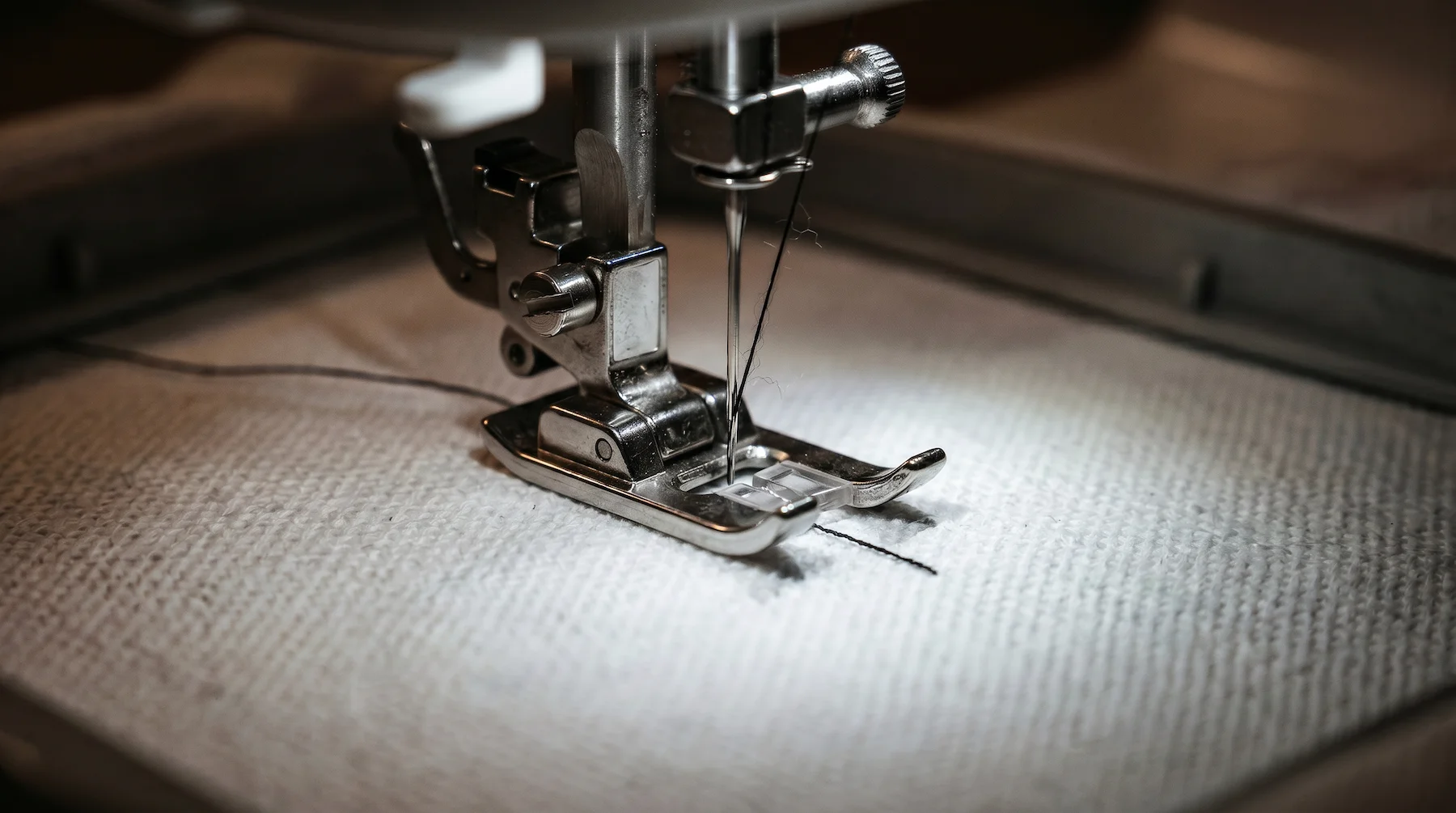 Macro shot of an embroidery machine needle precisely stitching a custom minimalist black line design onto a Blnk white cotton t-shirt.